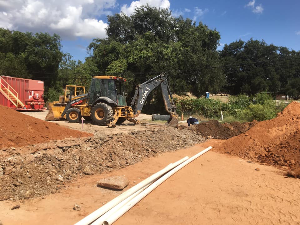 Backhoe digging a septic drain field trench with pipe staged nearby on a Hood County property